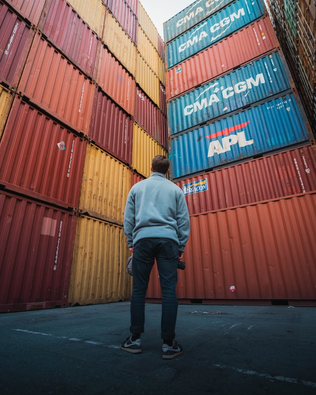 Man looks up at large stacks of shipping containers, he is almost surrounded by them.